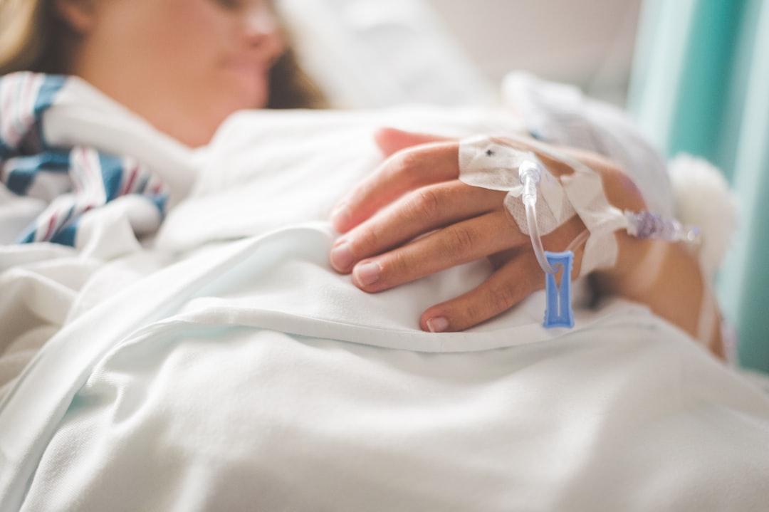 A woman laying in a hospital bed with an iv in her hand from Stephen Andrews on Unsplash