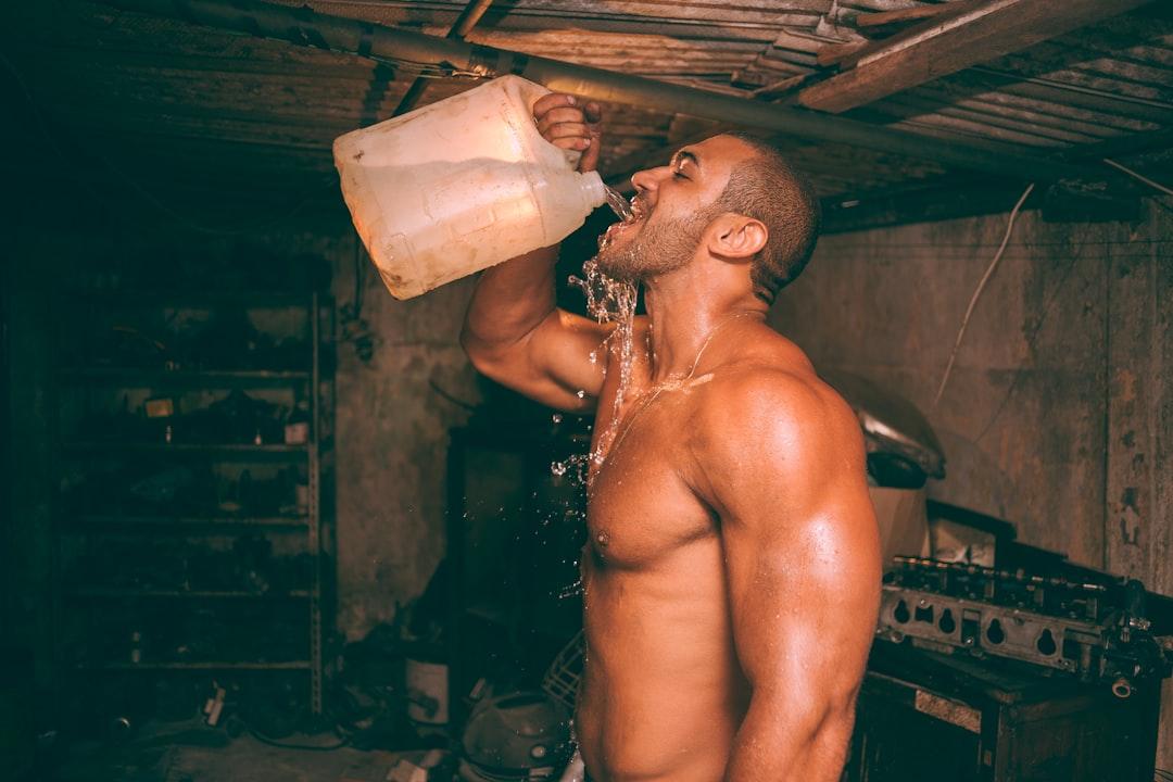 Topless man drinking water from plastic container from henri meilhac on Unsplash