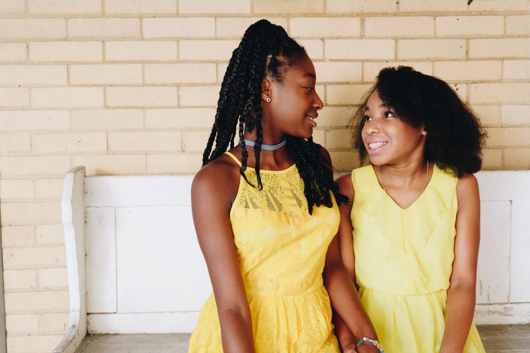 Two girl's in yellow sleeveless dresses sitting on white wooden bench during daytime from Eye for Ebony on Unsplash