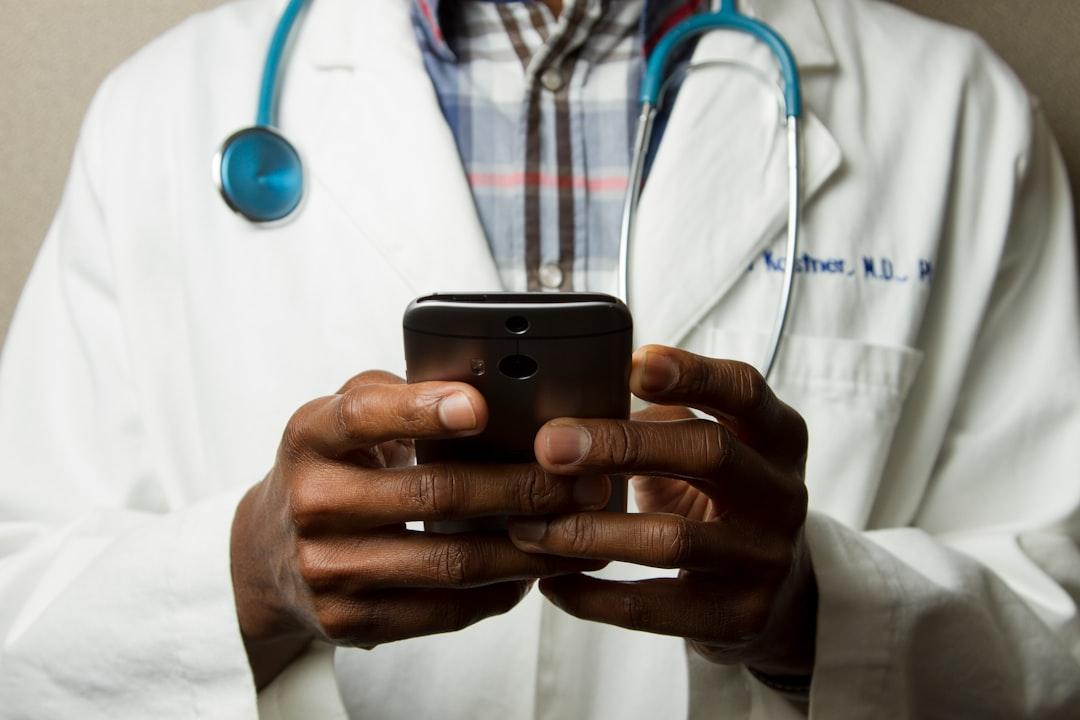 Person wearing lavatory gown with green stethoscope on neck using phone while standing from National Cancer Institute on Unsplash