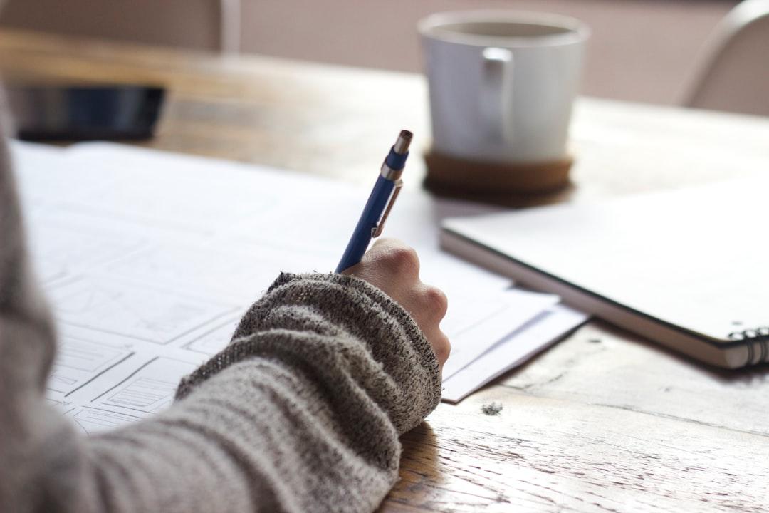 Person writing on brown wooden table near white ceramic mug from Unseen Studio on Unsplash