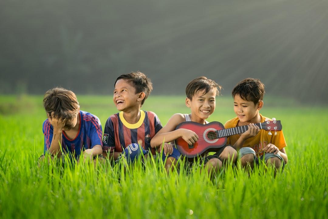 Four boys laughing and sitting on grass during daytime from Robert Collins on Unsplash SMS gây ảnh hưởng tới não của trẻ em