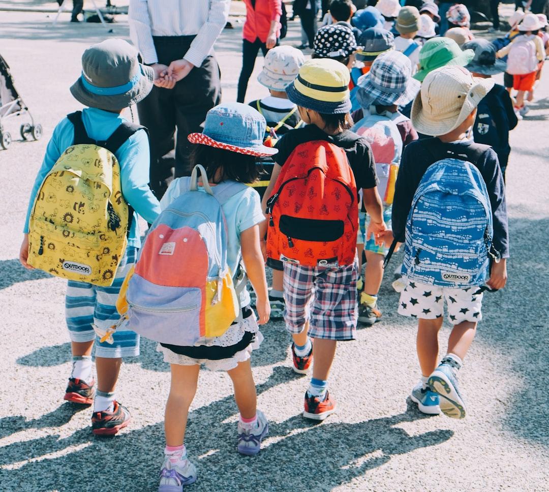Group of people wearing white and orange backpacks walking on gray concrete pavement during daytime from note thanun on Unsplash