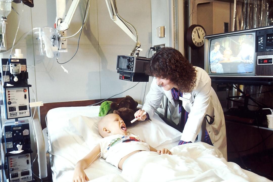 Child lying on bed while doctor checking his mouth from National Cancer Institute on Unsplash Phòng bệnh cho trẻ lúc giao mùa