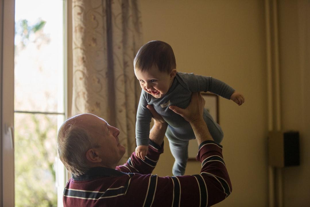 Man wearing maroon, white, and blue stripe long-sleeved shirt lifting up baby wearing gray onesie from Johnny Cohen on Unsplash Bệnh loãng xương
